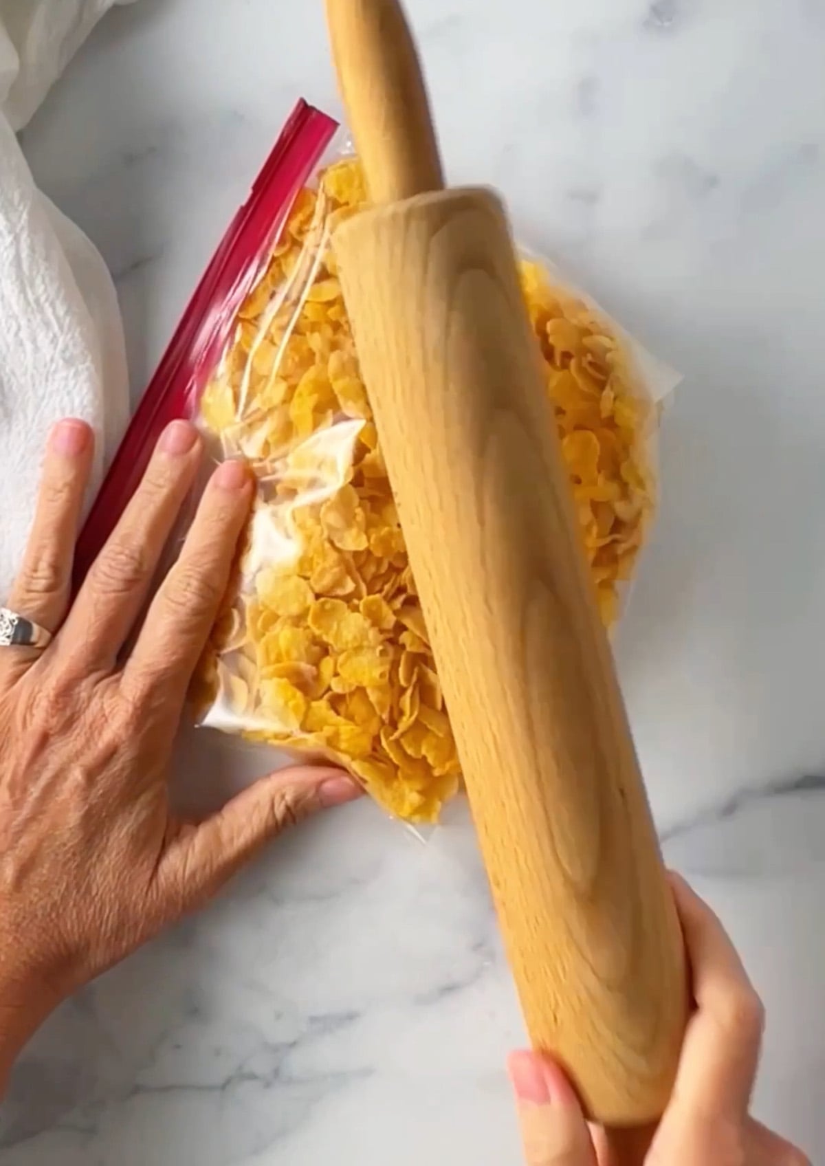 Using a rolling pin to crush corn flakes in a plastic bag.