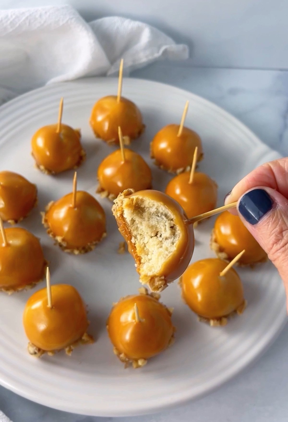 Apple-flavored butter cookie balls decorated to look like mini caramel apples with toothpicks on top, one cookie showing a bite taken out.