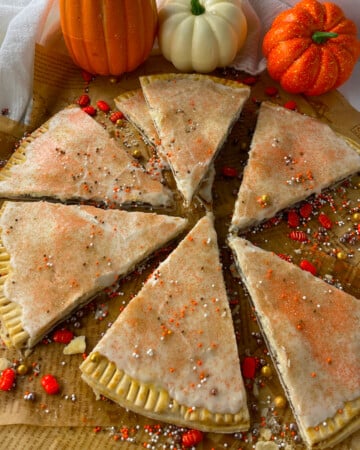 Homemade pumpkin pie pop tarts cut into pie shapes on parchment paper.