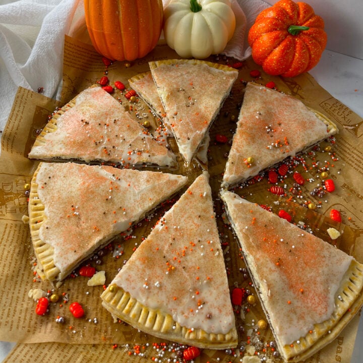 Homemade pumpkin pie pop tarts cut into pie shapes on parchment paper.