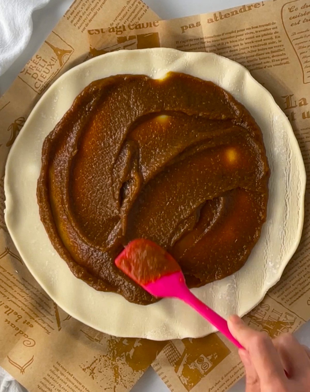 Spreading pumpkin pie filling onto round pie dough.