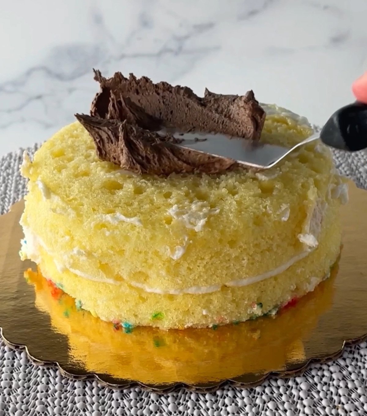 Frosting a yellow cake with chocolate frosting.