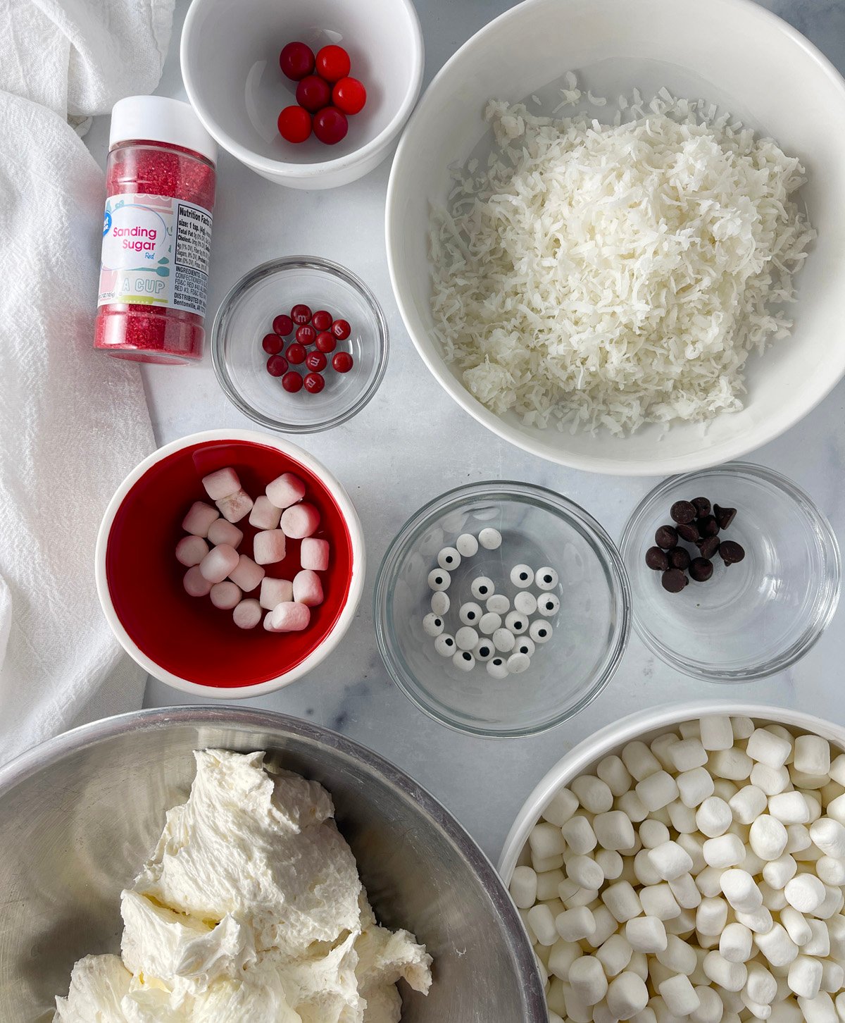 Bowls filled with red sanding sugar, chocolate chips, coconut, and candy for decorating Santa cookies.