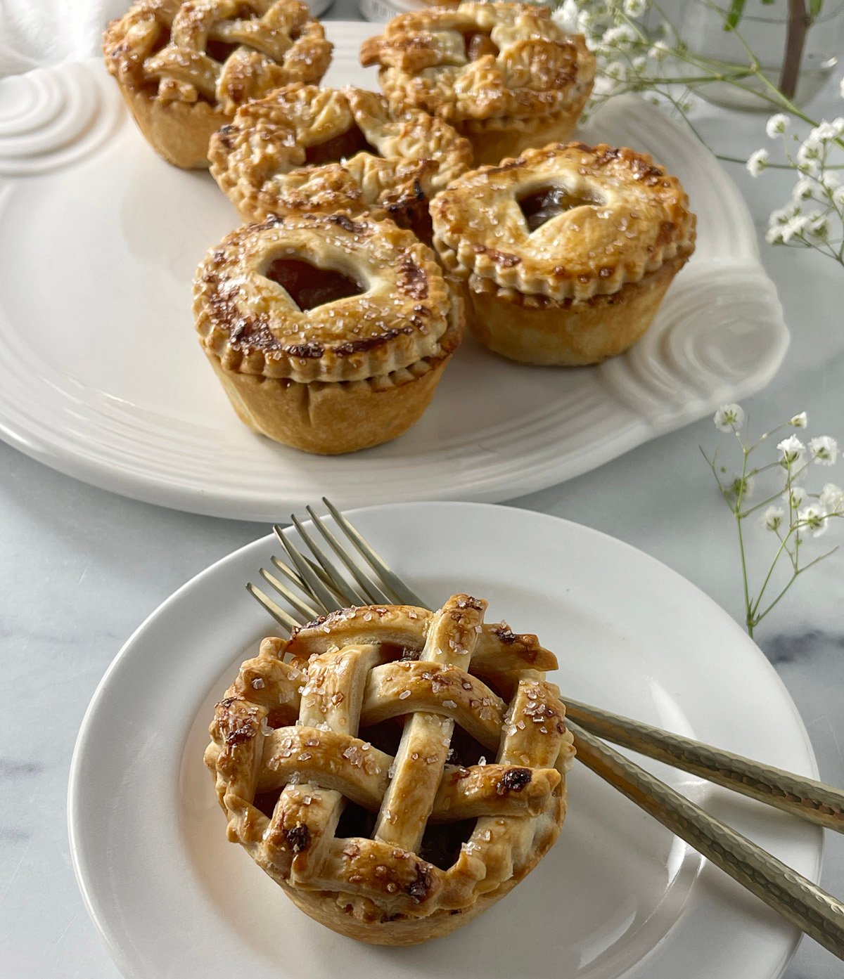 Plated caramel apple mini pie on a white plate with more mini pies blurred in the background.