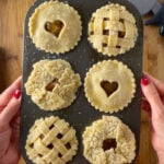 Muffin pan filled with unbaked mini caramel apple pies featuring lattice, heart, and leaf pie crust designs.