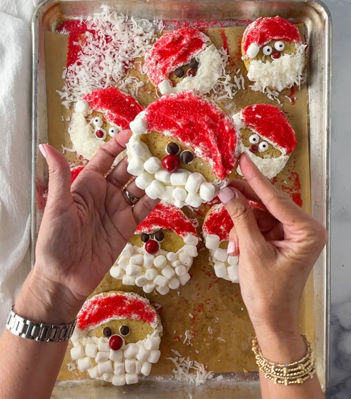 Hand holding a gluten-free Santa sugar cookie over a baking sheet of decorated Santa cookies.