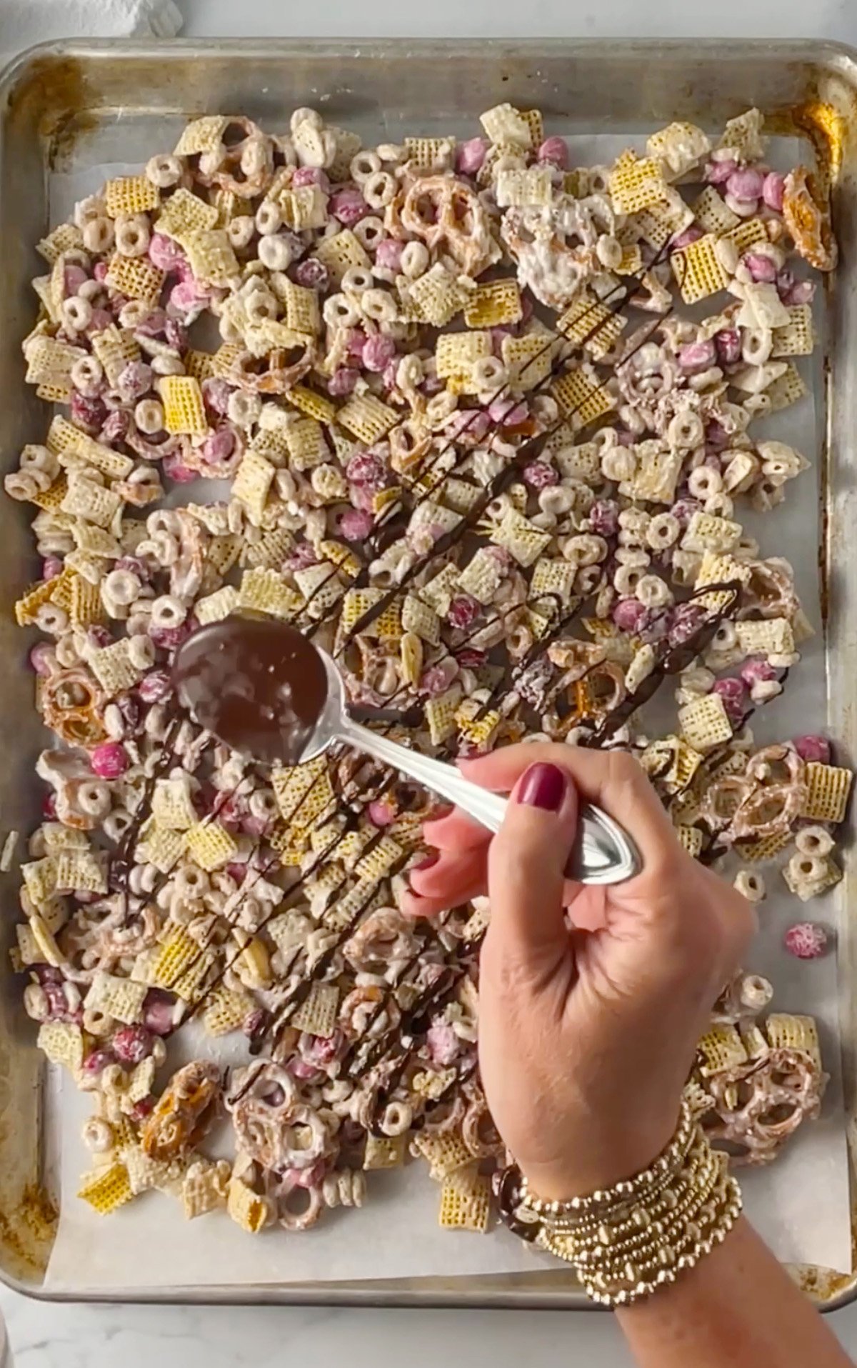 Drizzling melted chocolate over tray of snack mix.