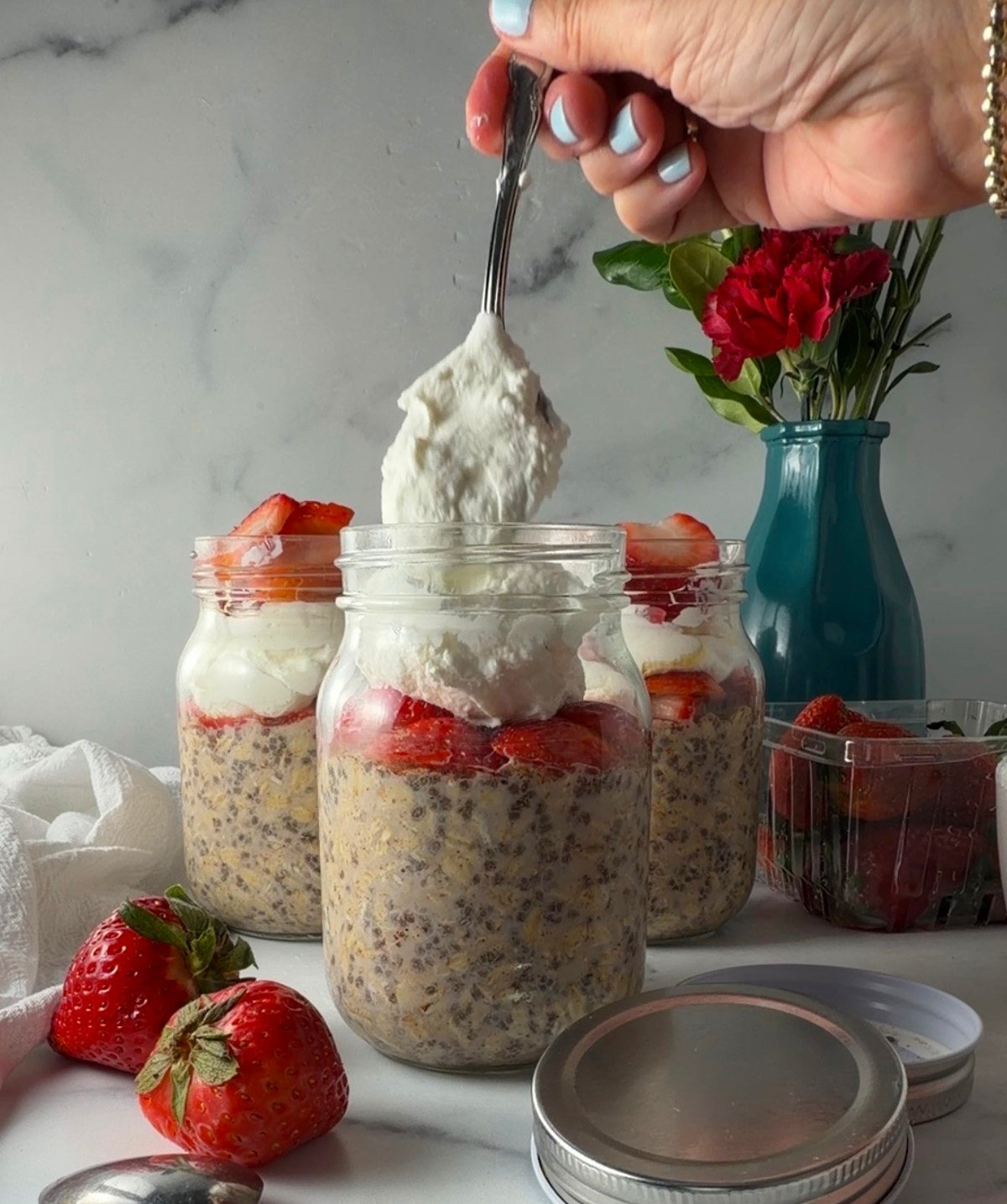 Scooping yogurt into jar of overnight oats with berries.