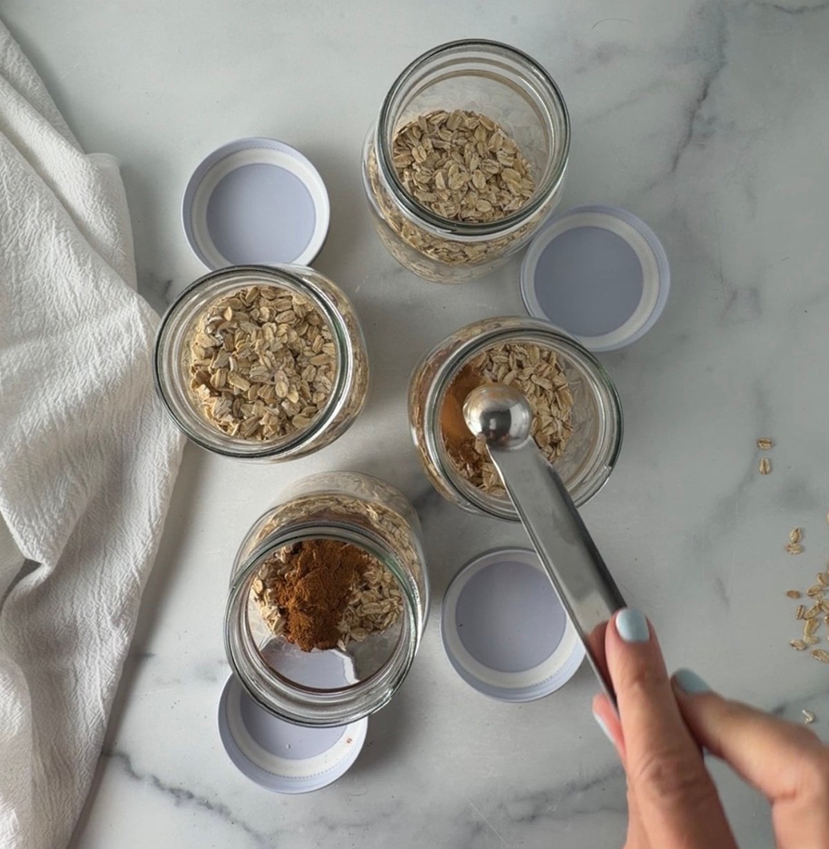 Four mason jars filled with oats, milk, chia seeds, and cinnamon ready to chill overnight.