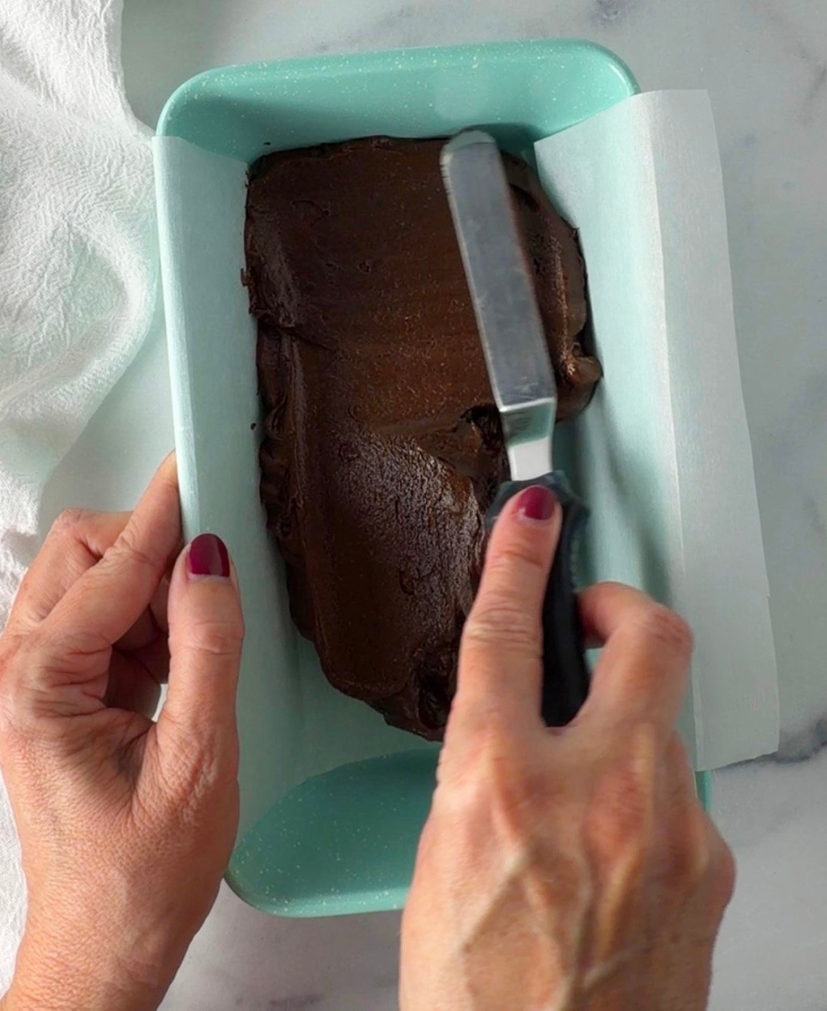 Spreading fudge mixture into parchment lined loaf pan.