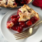 Cherry pie slice on white plate with gold fork.