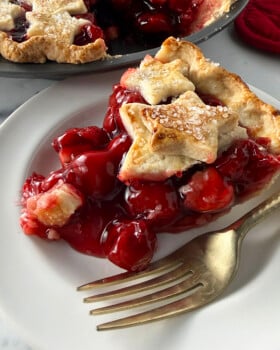 Cherry pie slice on white plate with gold fork.