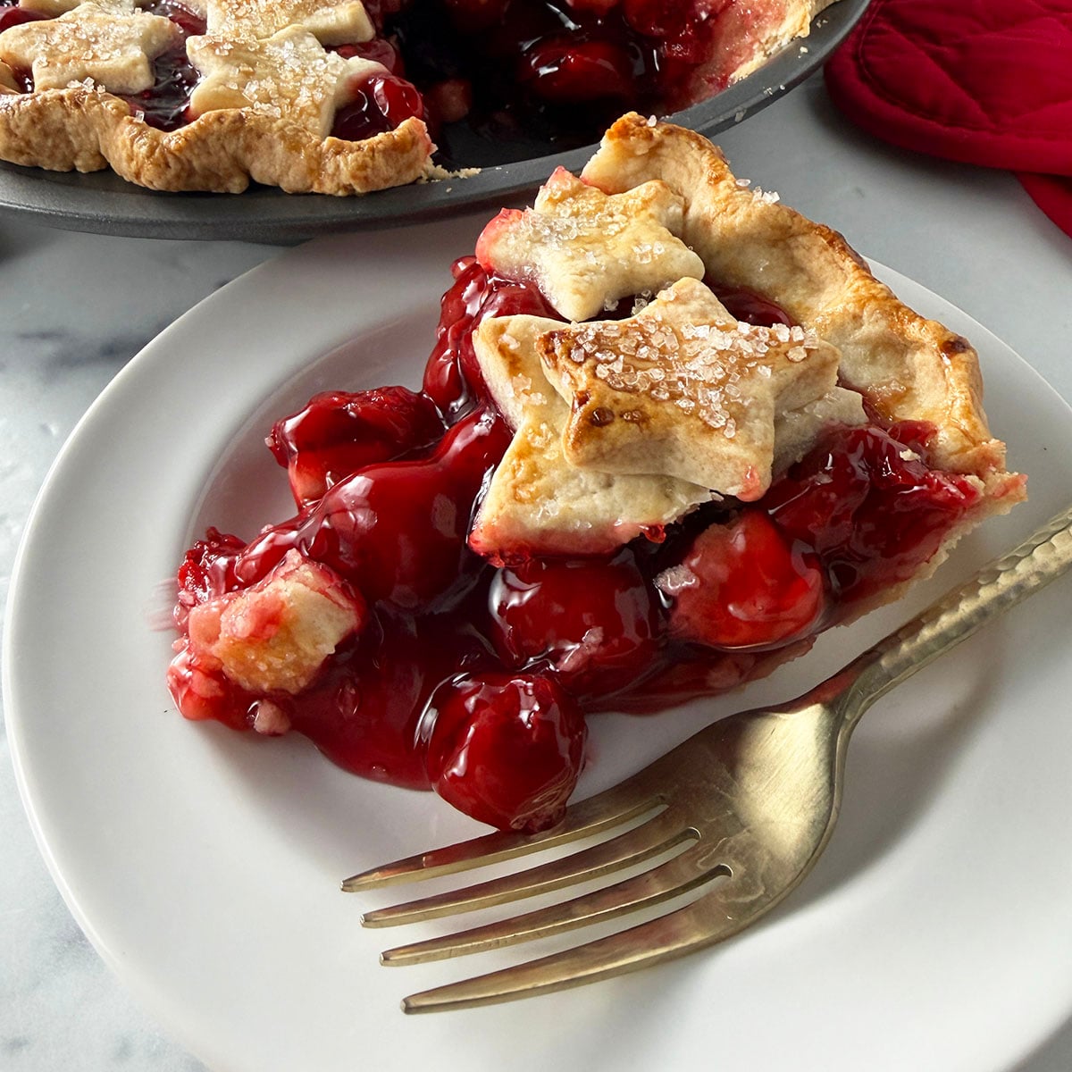 Cherry pie slice on white plate with gold fork.