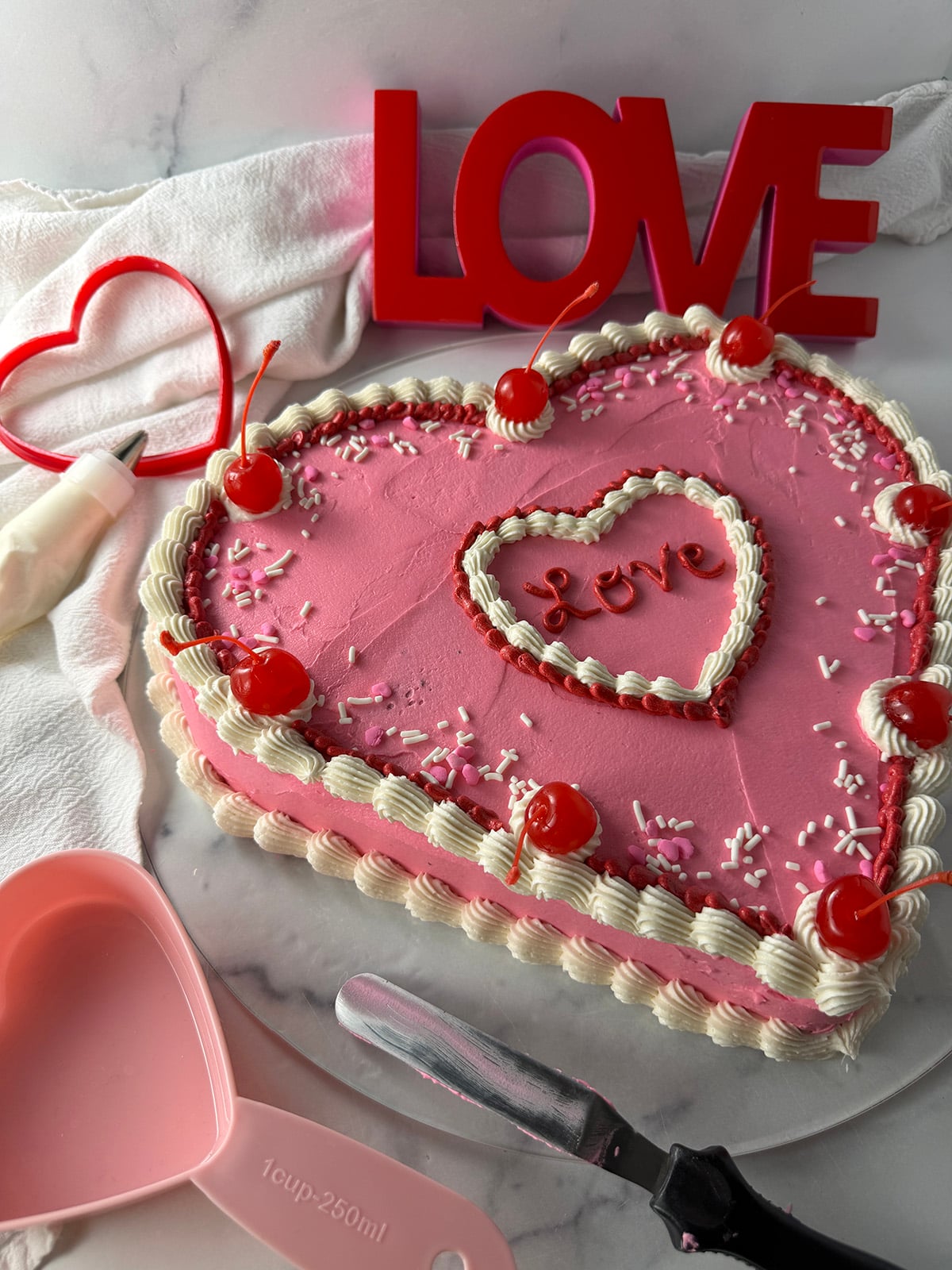Heart shaped chocolate cake with pink frosting and LOVE piped on top.