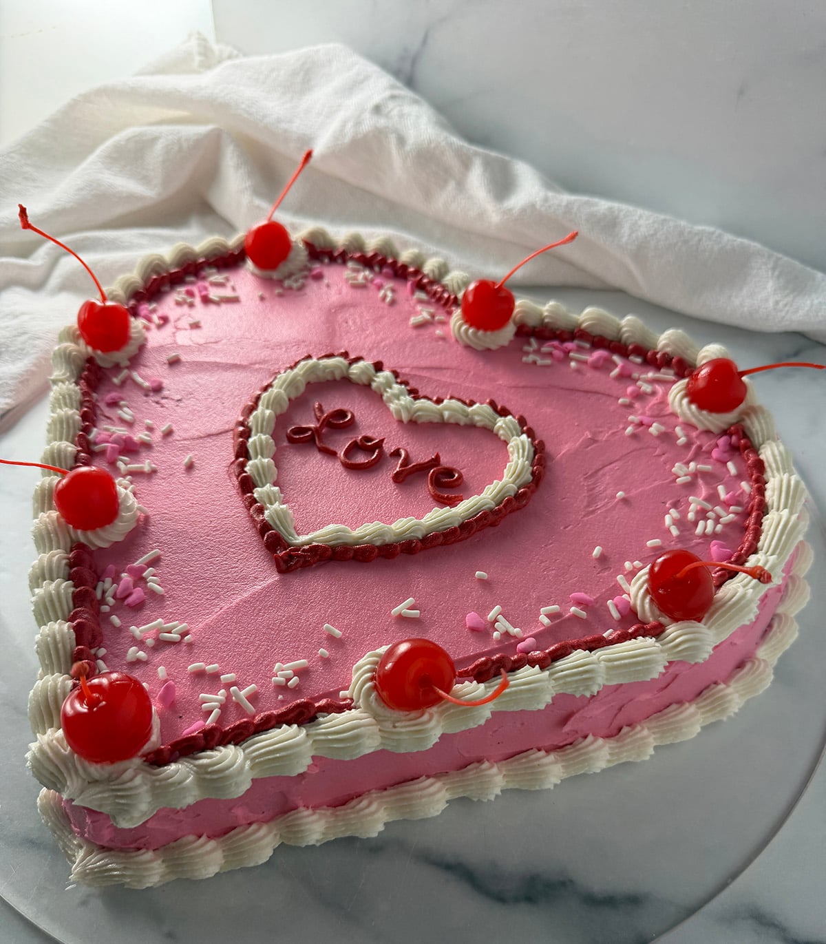 Beautiful heart shaped cake with pink frosting, maraschino cherries and white piping.