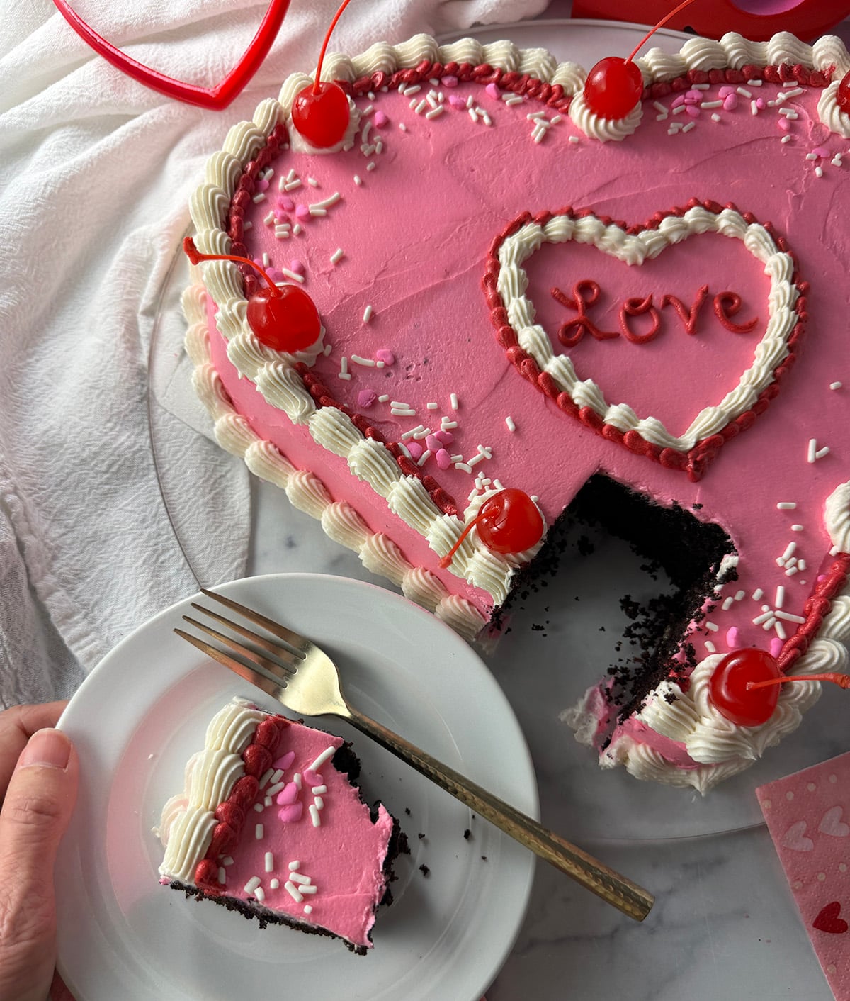 Heart shaped chocolate cake with pink frosting and slice taken out.