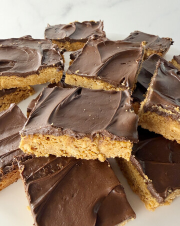 Old fashioned chocolate peanut butter bars stacked up on a plate in a pile.